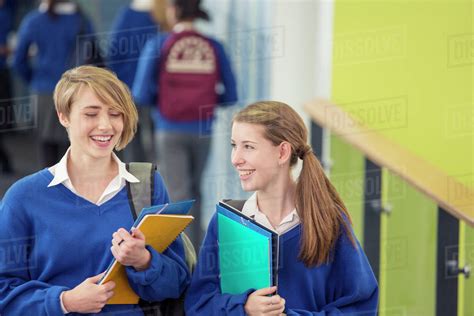 Two smiling female students wearing school uniforms walking through school corridor - Stock ...