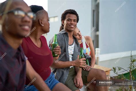 Portrait confident young man drinking beer with friends on patio ...