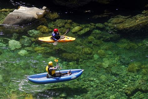 two people in kayaks paddling on the water with rocks and green algaes