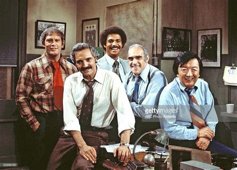 a group of men standing next to each other in front of a desk and chair