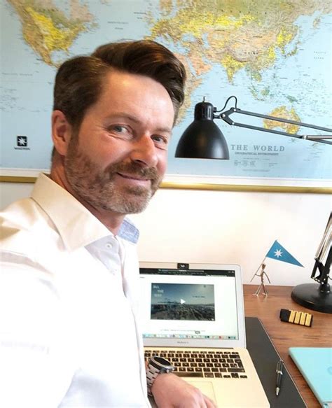 a man sitting at a desk with a laptop computer in front of him and a world map on the wall ...