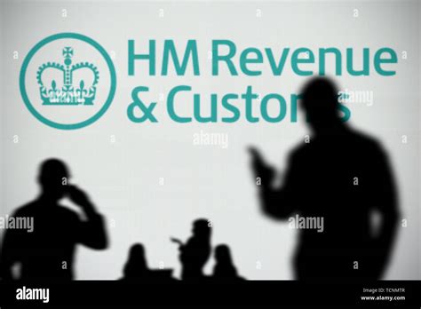 The HMRC logo is seen on an LED screen in the background while a silhouetted person uses a ...