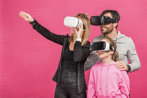 family using virtual reality headsets together, isolated on pink - Stock Photo - Dissolve