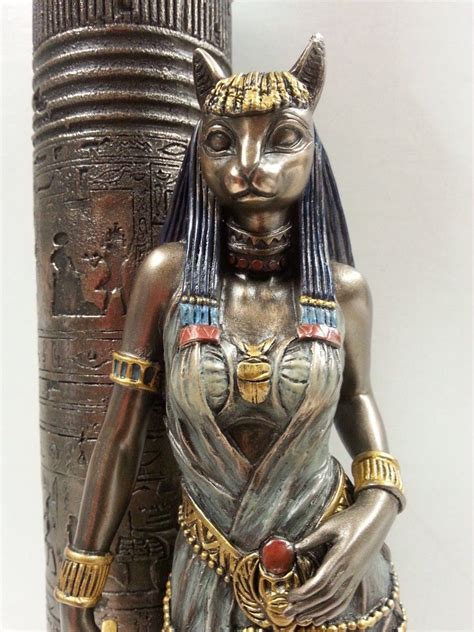 a statue of an egyptian woman next to a large metal pillar with gold decorations on it