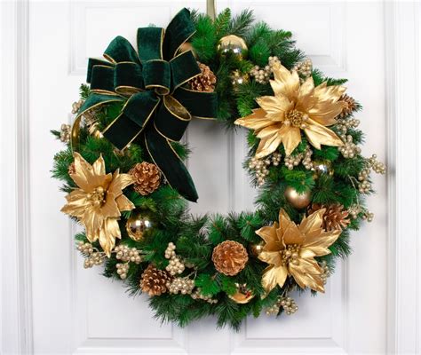 a green wreath with gold poinsettis and pine cones hanging on a white door