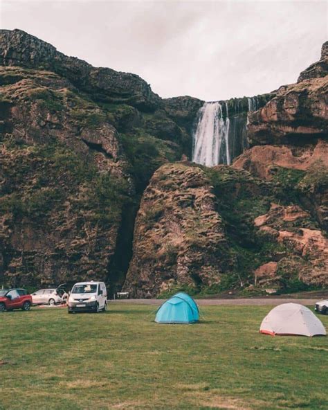 several tents pitched up in front of a waterfall with cars parked near ...