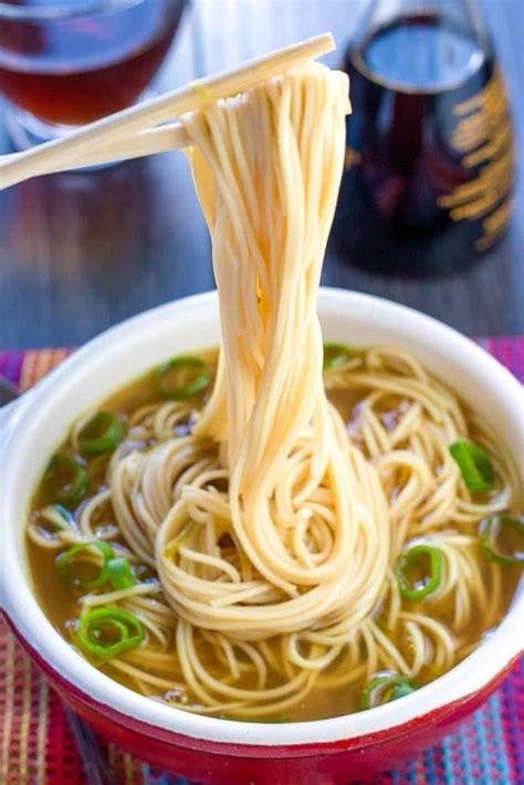 A bowl of quick and easy Chinese noodle soup with chopsticks holding some noodles above the bowl ...