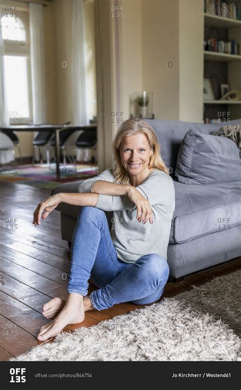 Portrait of smiling mature woman siiting barefoot on the floor in the ...