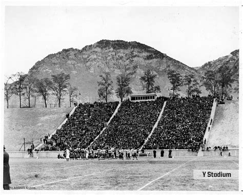 an old black and white photo of a football stadium with mountains in the back ground