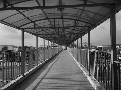 black and white photograph of a person walking down a walkway with a metal roof over it