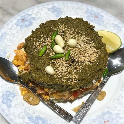 a white plate topped with a green cake covered in nuts and veggies next ...