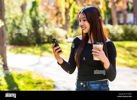 A young Chinese International student stands holding a coffee cup and ...