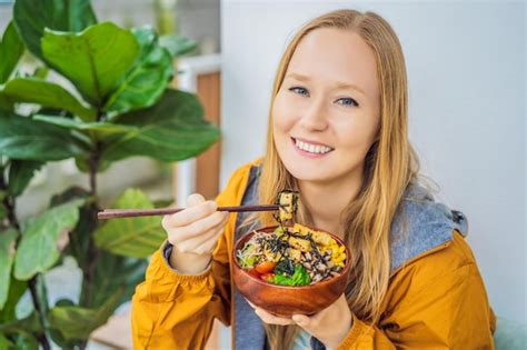 Premium Photo | Woman eating raw organic poke bowl with rice and veggies closeup on the table ...