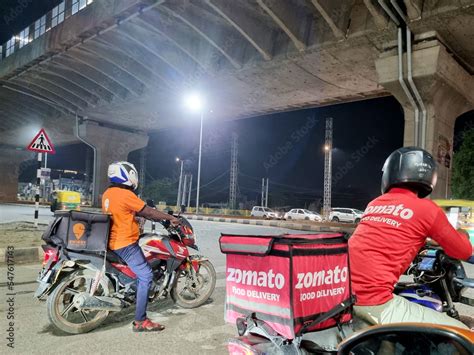 Zomato bike rider delivery boy looking at rider from swiggy food tech starup apps showing ...