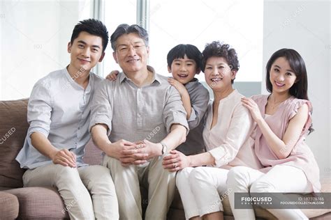 Portrait of happy Chinese family of three generations sitting on sofa ...