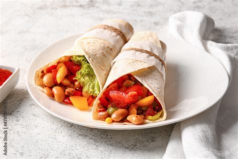 Plate of tasty Mexican burritos with vegetables on light background ...