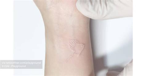 Minimalistic white bird tattoo located on the wrist.