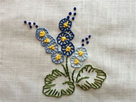 a blue and yellow flower is on a white cloth with green leafy stems in ...