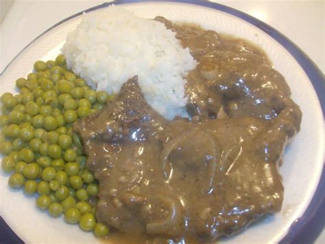 a white plate topped with meat, peas and gravy on top of rice