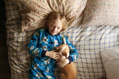 Overhead shot of smiling boy sleeping with dog on bed stock photo