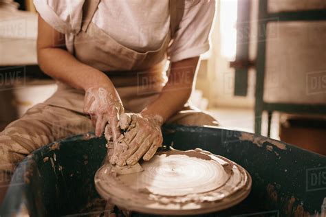 Woman flattening clay on pottery wheel in workshop. Craftswoman working on clay with flattening ...