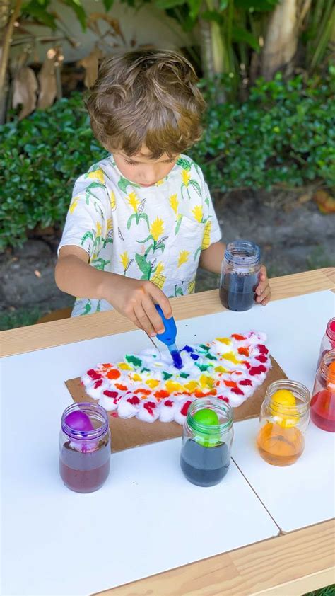 a little boy that is standing in front of a table with some paints on it