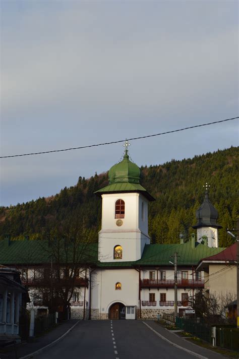 a white building with a green roof on the side of a road in front of a mountain