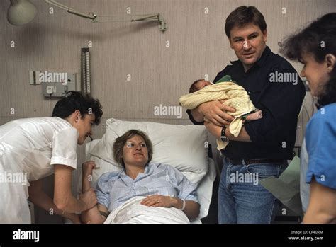 Woman after giving birth in hospital looking on to partner holding ...