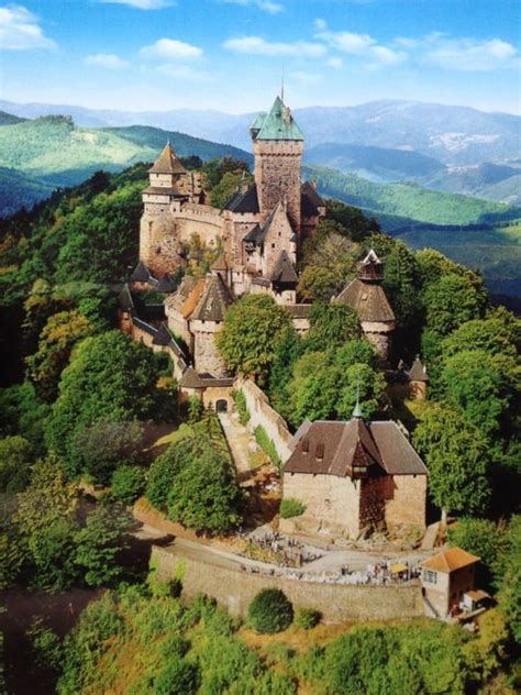 an old castle on top of a hill surrounded by trees and mountains in the background