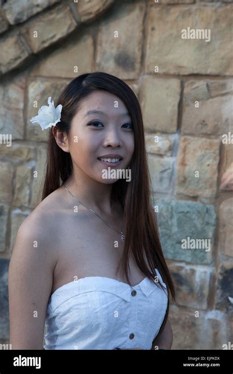 Pretty Asian woman outdoors by a stone wall, in a white dress and with ...