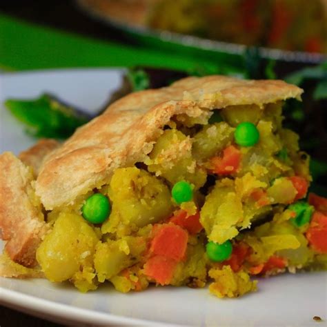 a piece of vegetable pie on a plate with peas and carrots in the background