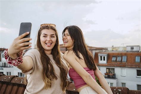 Happy women sticking out tongue while taking selfie through smart phone on rooftop stock photo