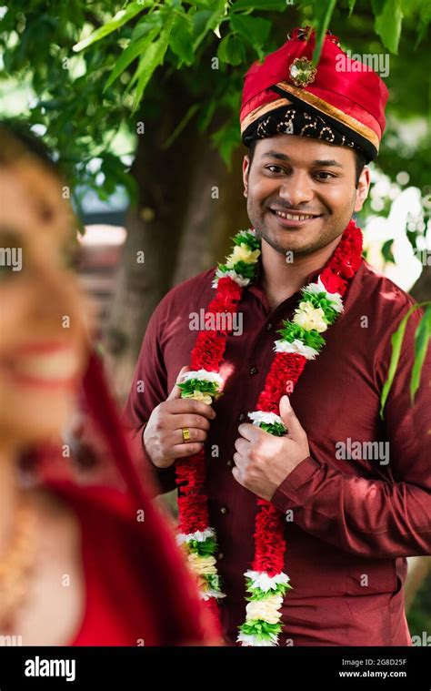 happy indian man in turban and floral garland looking at blurred bride ...