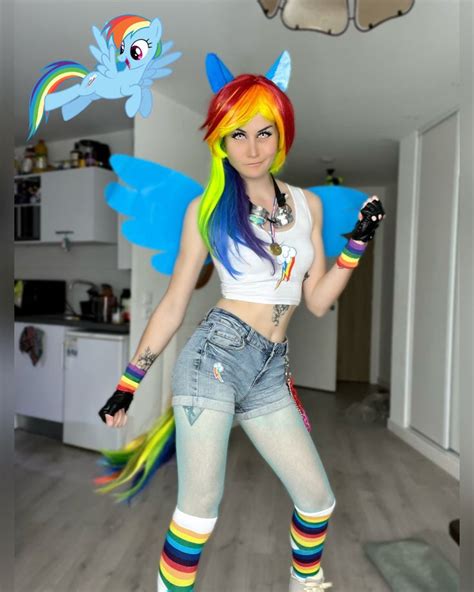 a woman with rainbow hair and blue shorts is posing for the camera while holding a cell phone