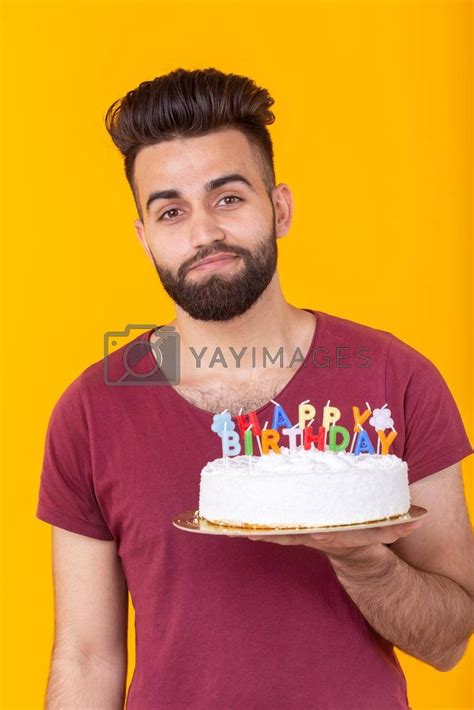 a man holding a cake with candles on it in front of an orange wall and yellow background
