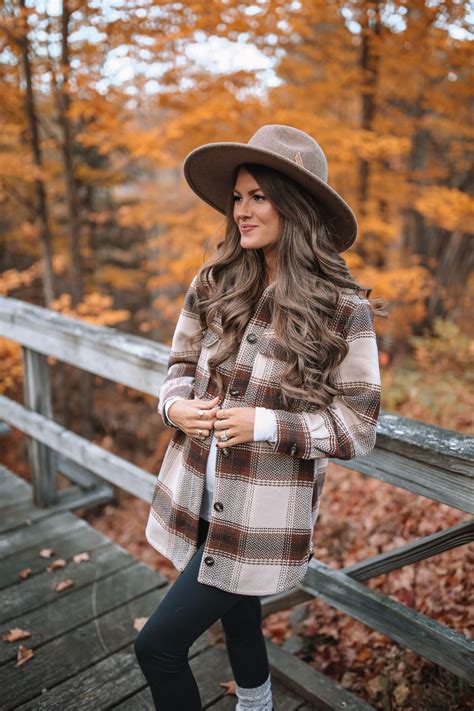 a woman standing on a wooden bridge wearing a hat and coat with her hands in her pockets