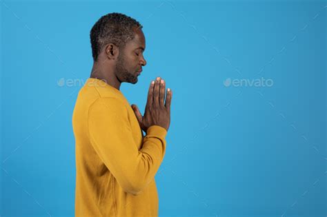 Black man praying with closed eyes on blue, side view Stock Photo by Prostock-studio