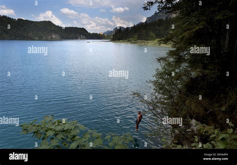 15 August 2023, Bavaria, Schwangau: A young man jumps from the steep bank into the turquoise ...