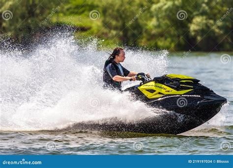 Young Caucaisian Woman Drives BRP Sea-Doo Jet Ski Splashing at Sunset by River Bank at ...