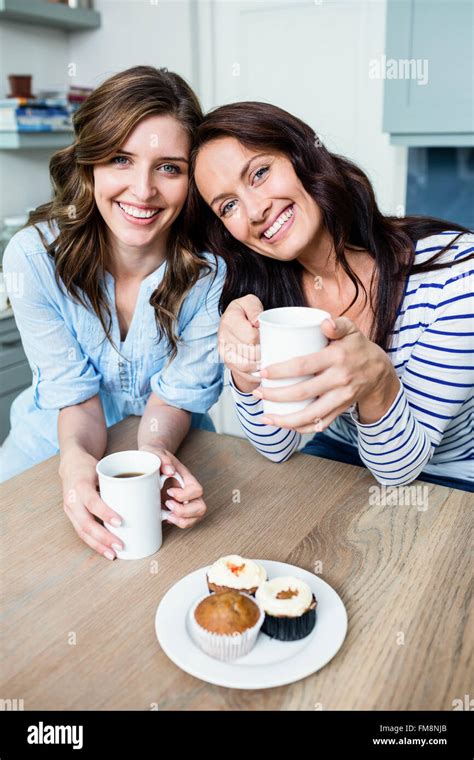 Smiling female friends holding coffee mugs at table Stock Photo - Alamy