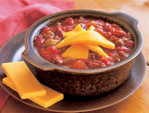 a bowl filled with chili and cheese on top of a wooden table next to a ...