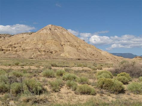 a large hill in the middle of a desert with shrubs and bushes around it ...