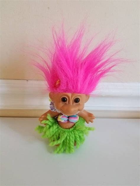 a troll doll with pink hair and green skirt on top of a white countertop