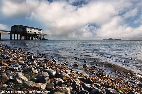 a beach with rocks and pebbles on the shore under a cloudy blue sky, next to a pier