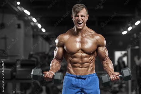 Muscular man working out in gym doing exercises with dumbbells, strong male naked torso abs foto ...