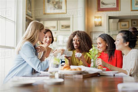 Smiling women drinking coffee and talking at restaurant table - Stock Photo - Dissolve