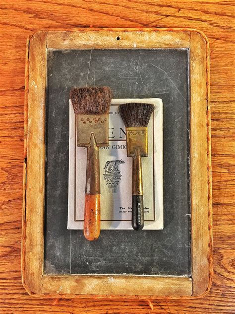 two brushes sitting on top of a piece of paper next to a wooden frame ...