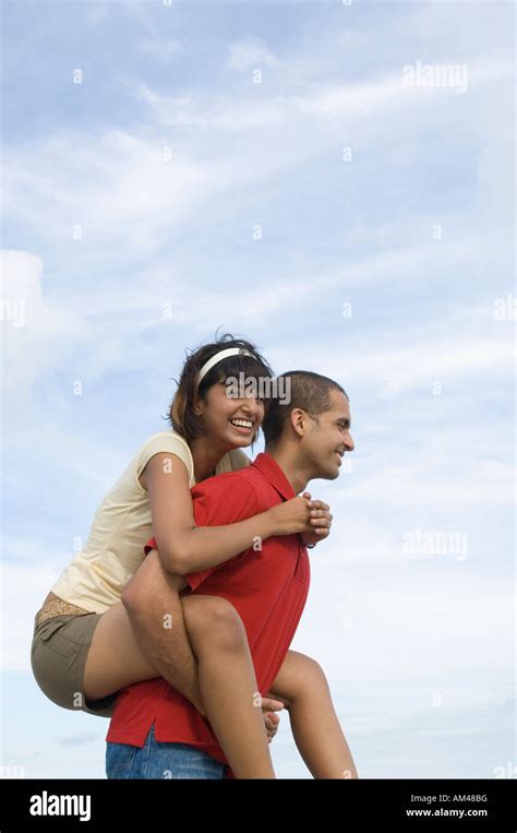 Portrait of a young woman riding piggyback on a young man and smiling Stock Photo - Alamy