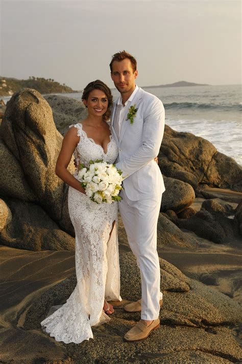 a bride and groom posing on the rocks by the water at their beach wedding ceremony