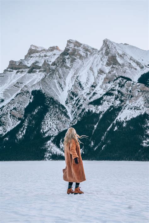 a woman standing on top of a snow covered field with mountains in the back ground